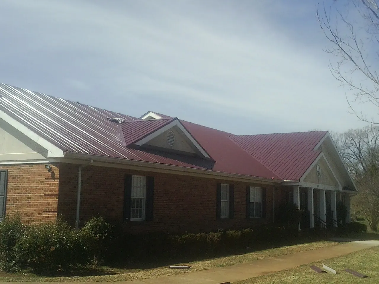 Red metal roof with gabled entries on a long brick building, from a Hail Damage Roof Repair job in Rincon