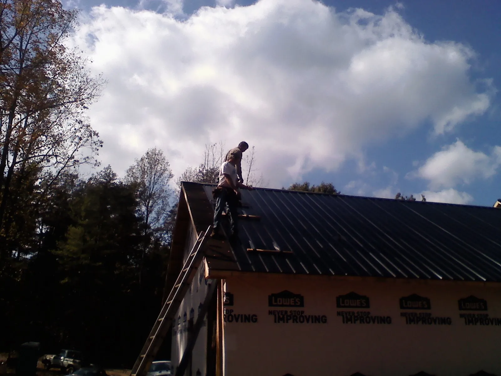 Roofer fastening dark metal panels high against a cloudy sky, from a Roof Inspection job in Rincon
